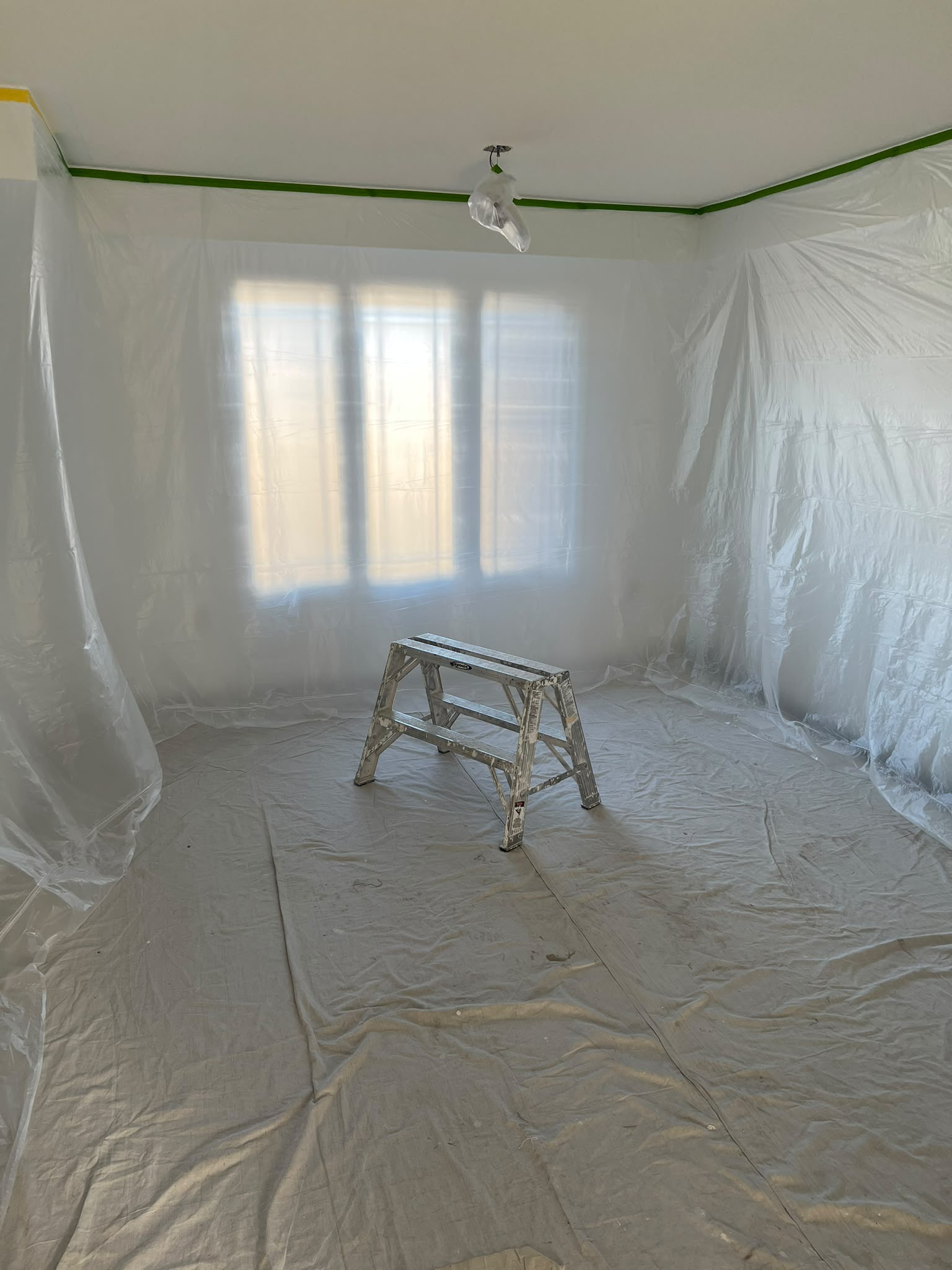Room prepared for ceiling work with walls and windows covered in sheeting and floors protected